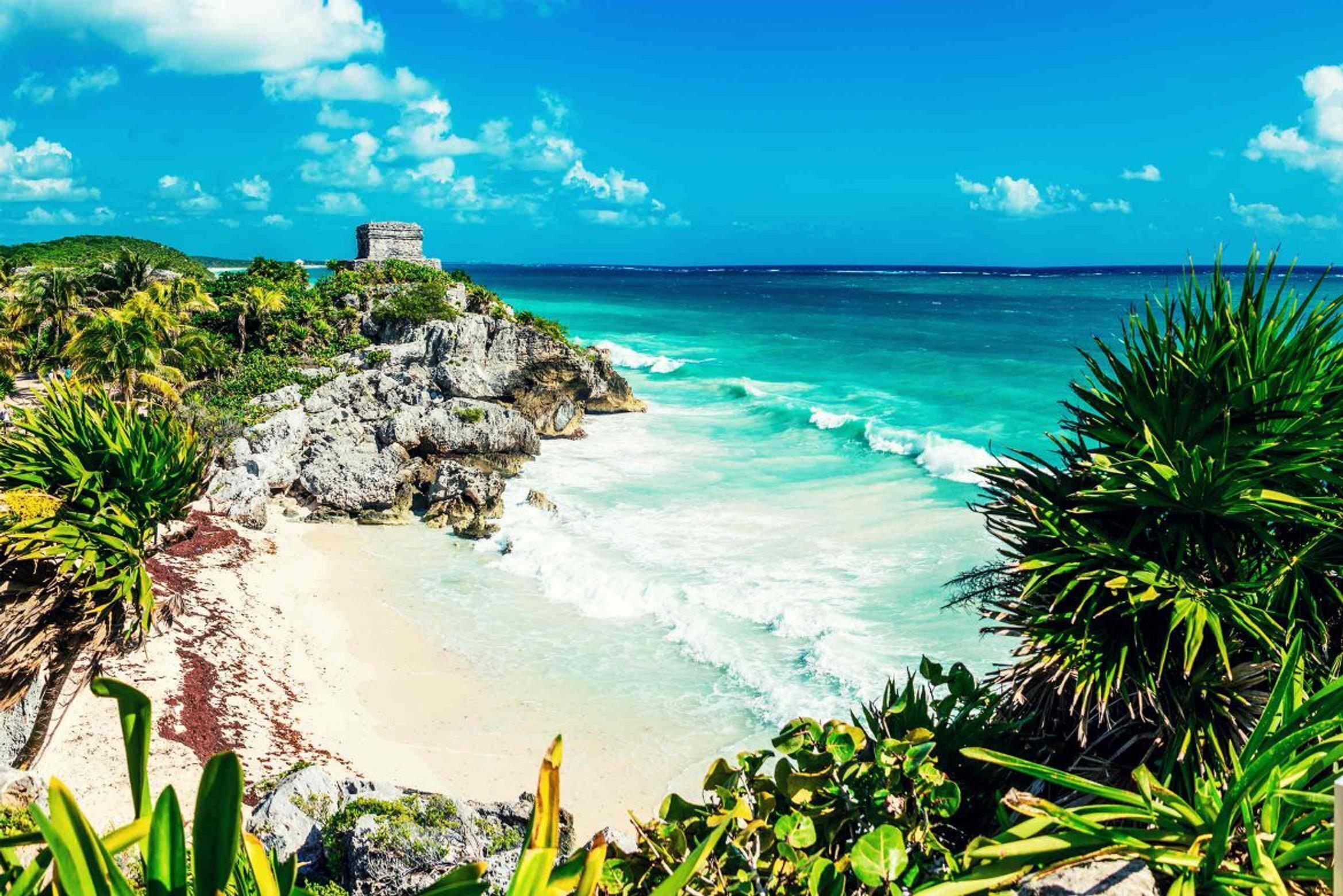 A beach with clear turquoise waters, a rocky shoreline, and a small ancient structure.