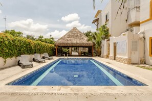 A swimming pool with lounge chairs, a thatched-roof gazebo, and a building with stone accents. - Nice Apartment & Pool in Playa del Carmen 8 Min From the Caribbean Sea (Playa del Carmen)