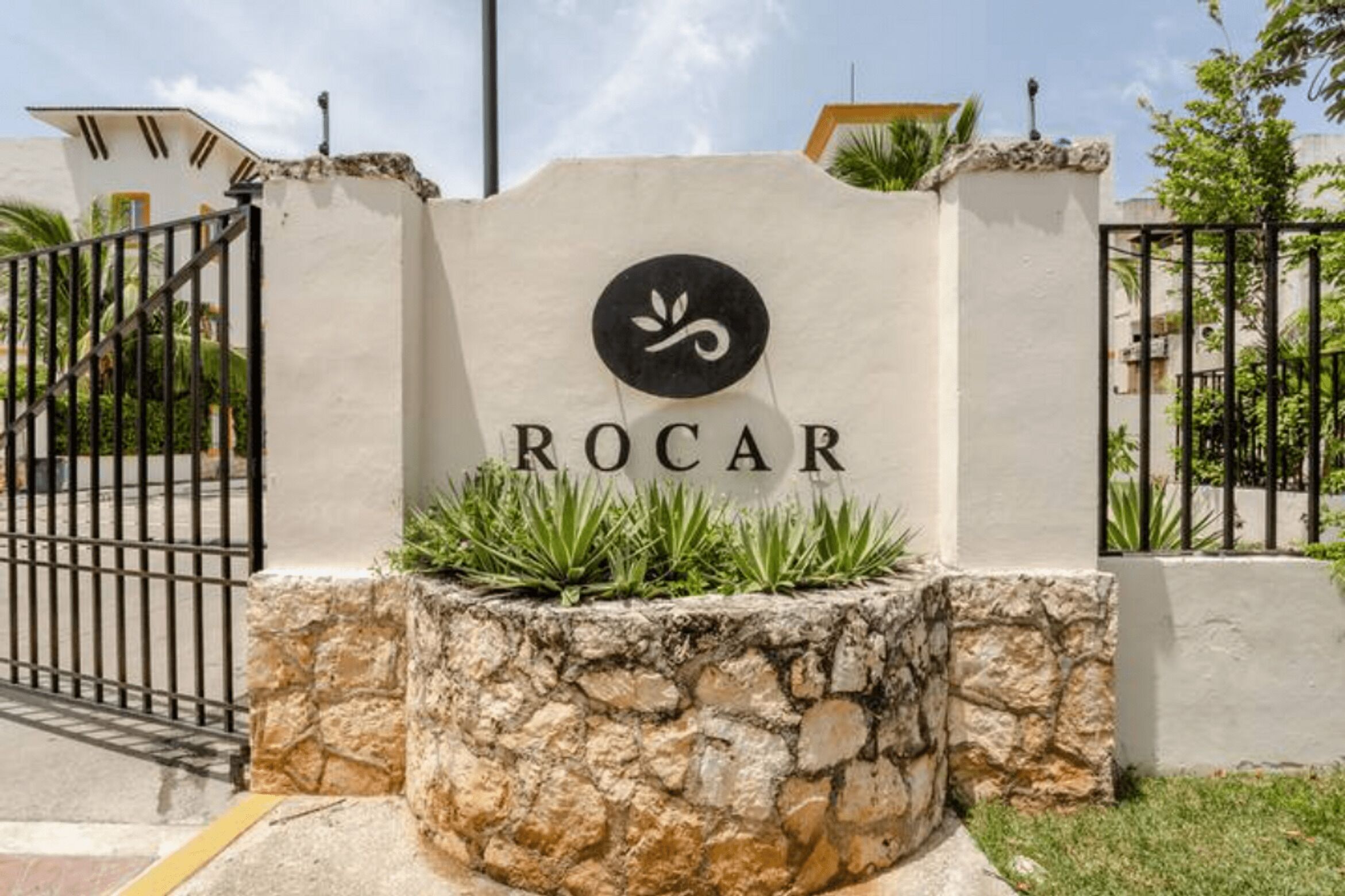 A sign with the name 'ROCAR' and a logo, surrounded by a stone wall and a metal gate.