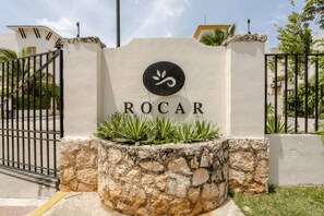 A sign with the name 'ROCAR' and a logo, surrounded by a stone wall and a metal gate. - Nice Apartment & Pool in Playa del Carmen 8 Min From the Caribbean Sea (Playa del Carmen)