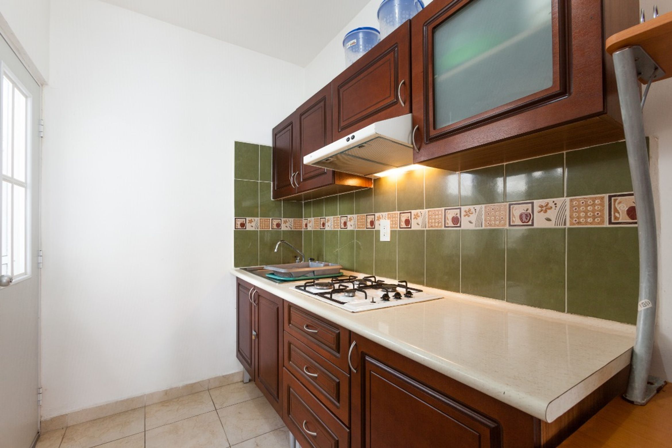 A kitchen with wooden cabinets, a gas stove, and green tiled backsplash.