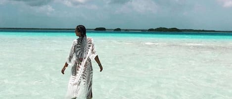 A person walking in clear turquoise water with a distant island and cloudy sky.