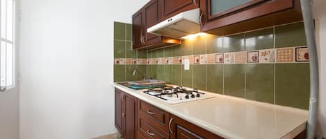 Una cocina con armarios de madera, estufa a gas y salpicadero de azulejos verdes.