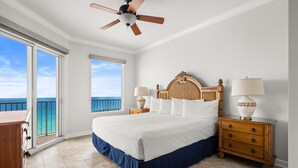 Ein Schlafzimmer mit einem Bett, zwei Nachttischen, einem Deckenventilator, Blick auf den Ozean und einer Holzkommode.