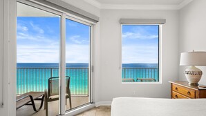 Ein Schlafzimmer mit Blick auf das Meer, einer Glastür, einem Holznachttisch und einem weißen Bett.