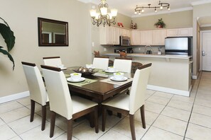 A dining area with a wooden table, white chairs, and a chandelier. - Ocean Villa 2305 (Panama City Beach)