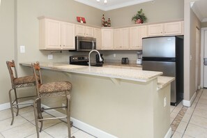 A kitchen with beige cabinetry, a central island with bar stools, a black refrigerator, a microwave, and a stove. - Ocean Villa 2305 (Panama City Beach)