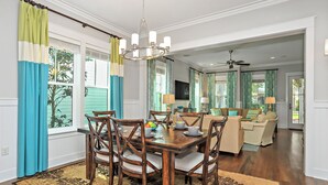 Un coin repas avec une table et des chaises en bois, un lustre et une vue sur le salon, où se trouvent un canapé et un téléviseur.