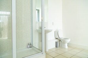 Een badkamer met een douchecabine van glas, een witte wastafel en een toilet.