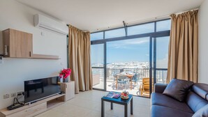 A modern living room with a flat-screen TV, a coffee table, a sofa, and a balcony with a view of the city.