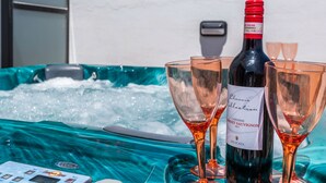 A bottle of wine and two glasses on a table with a hot tub in the background.