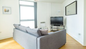 A modern living room with a grey sofa, a flat-screen TV, and a large window. - Kent Street - Apt 4 (Liverpool)