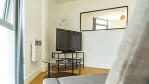 A modern living room with a flat-screen TV on a glass table, a sofa, and a large window. - Kent Street - Apt 4 (Liverpool)