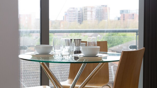 A dining table with chairs and a glass top, set with white dishes and glasses, overlooking a cityscape through large windows. - Kent Street - Apt 4 (Liverpool)