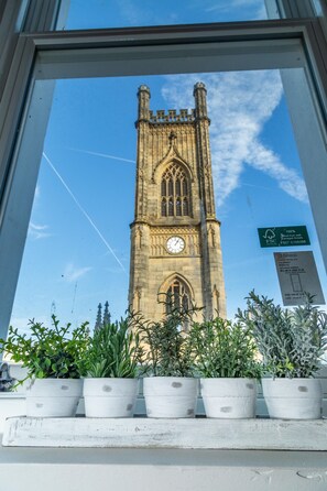 A view of a tall, historic tower with a clock, through a window with potted plants in front. - St Lukes Building (Liverpool)
