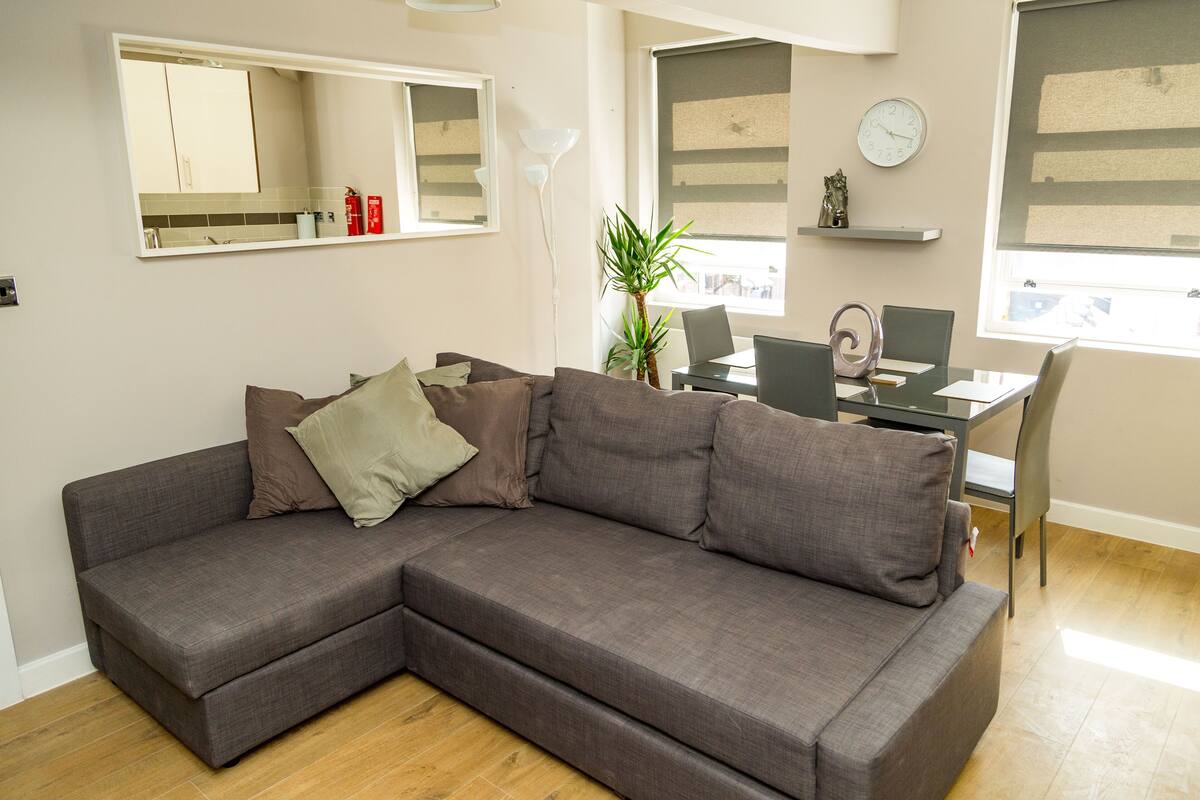 A modern living room with a sectional sofa, a dining table, and a small kitchen area.