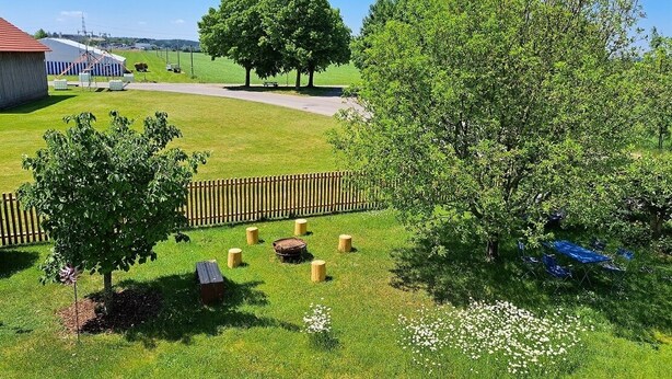 A grassy area with trees, a wooden fence, and a building with a red roof. - On the Allgäu cycle path, quiet apartment, with bicycle garage (Lachen-Hetzlinshofen)