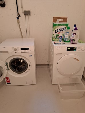 Un espace buanderie comprenant deux machines à laver, un distributeur de lessive TANDIL et une bouteille de lessive TANDIL.