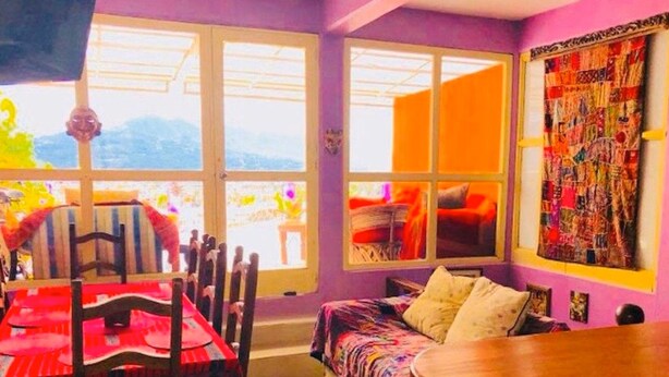 A room with a dining table, chairs, a sofa, and a large window with a view. - Amazing House of View (San Cristóbal de las Casas)
