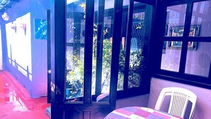A room with a round table and a white chair, a window with a view of greenery, and a door with a glass panel. - Amazing House of View (San Cristóbal de las Casas)