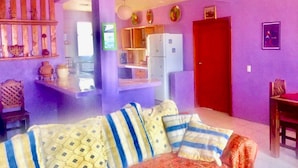 A living room with a sofa, a dining table, and a kitchen area with cabinets and a refrigerator. - Lindo Depa Chimenea Preciosa Vista (San Cristóbal de las Casas)