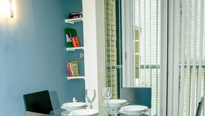 Ein Essbereich mit einem Glastisch, schwarzen Stühlen und einem Bücherregal an einer blauen Wand.