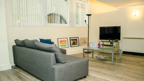 Ein modernes Wohnzimmer mit grauem Sofa, einem Glastisch und einem Flachbildfernseher.