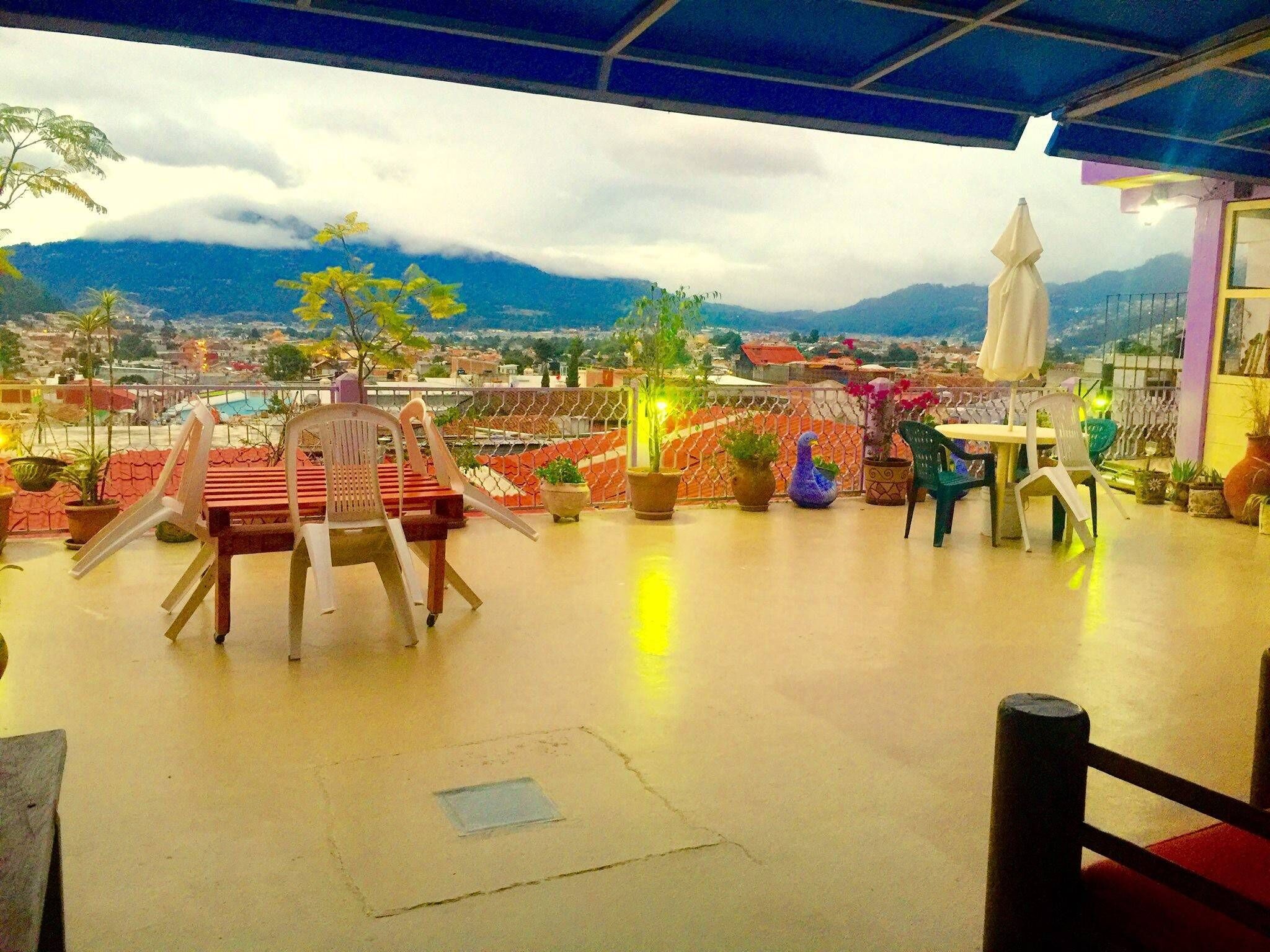 Une terrasse avec une table et des chaises, des plantes en pot, et une vue sur des montagnes lointaines et un paysage urbain.
