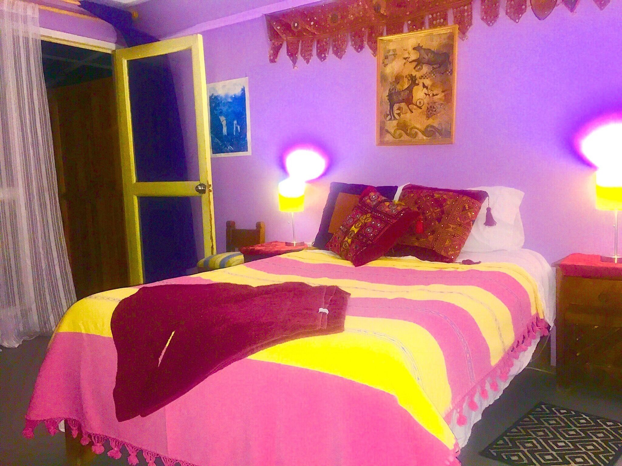 Un dormitorio con una cama, dos lámparas de noche, una puerta y un cuadro en la pared.
