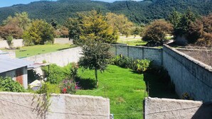 A courtyard with a view of a forested hill, surrounded by stone walls and greenery. - Comfy Bedroom Town House Garden Market Area (San Cristóbal de las Casas)