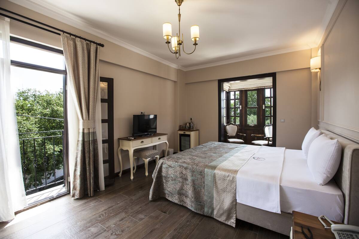 A hotel room with a bed, desk, television, and a view of greenery outside.