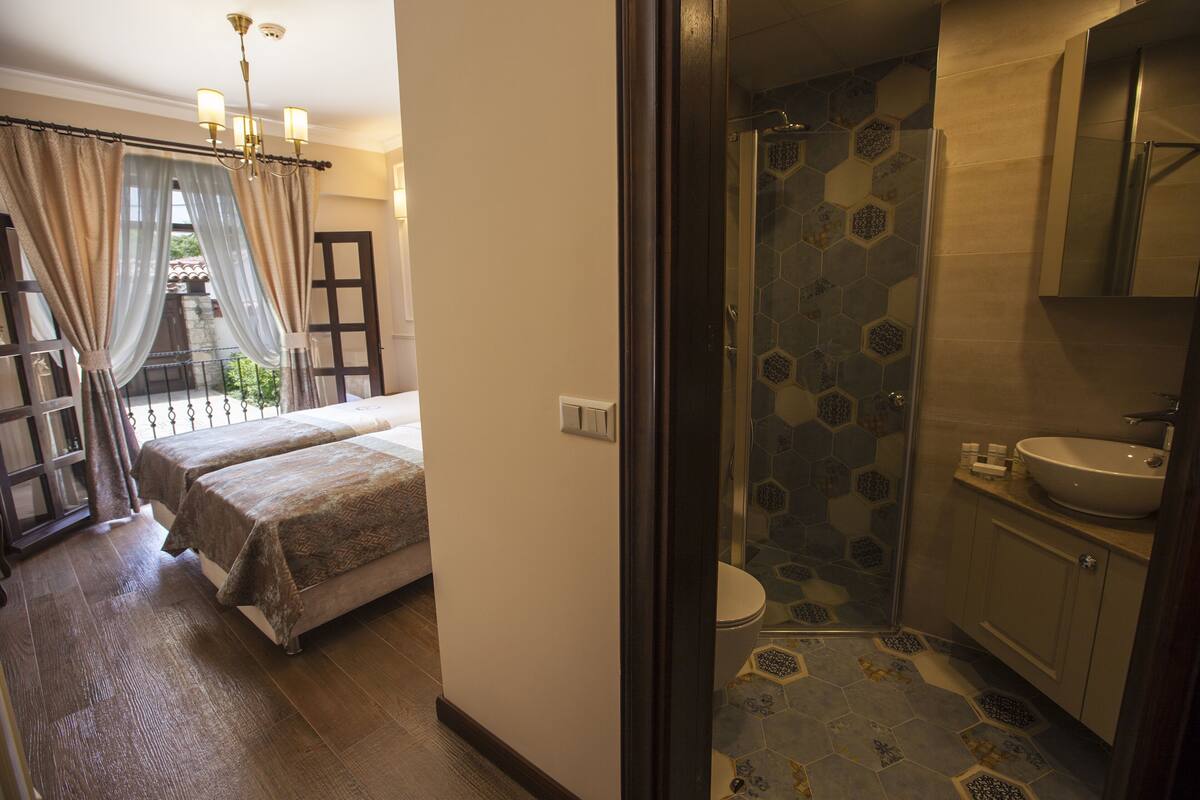 A bedroom with a bed, a bathroom with a shower, and a balcony with curtains.