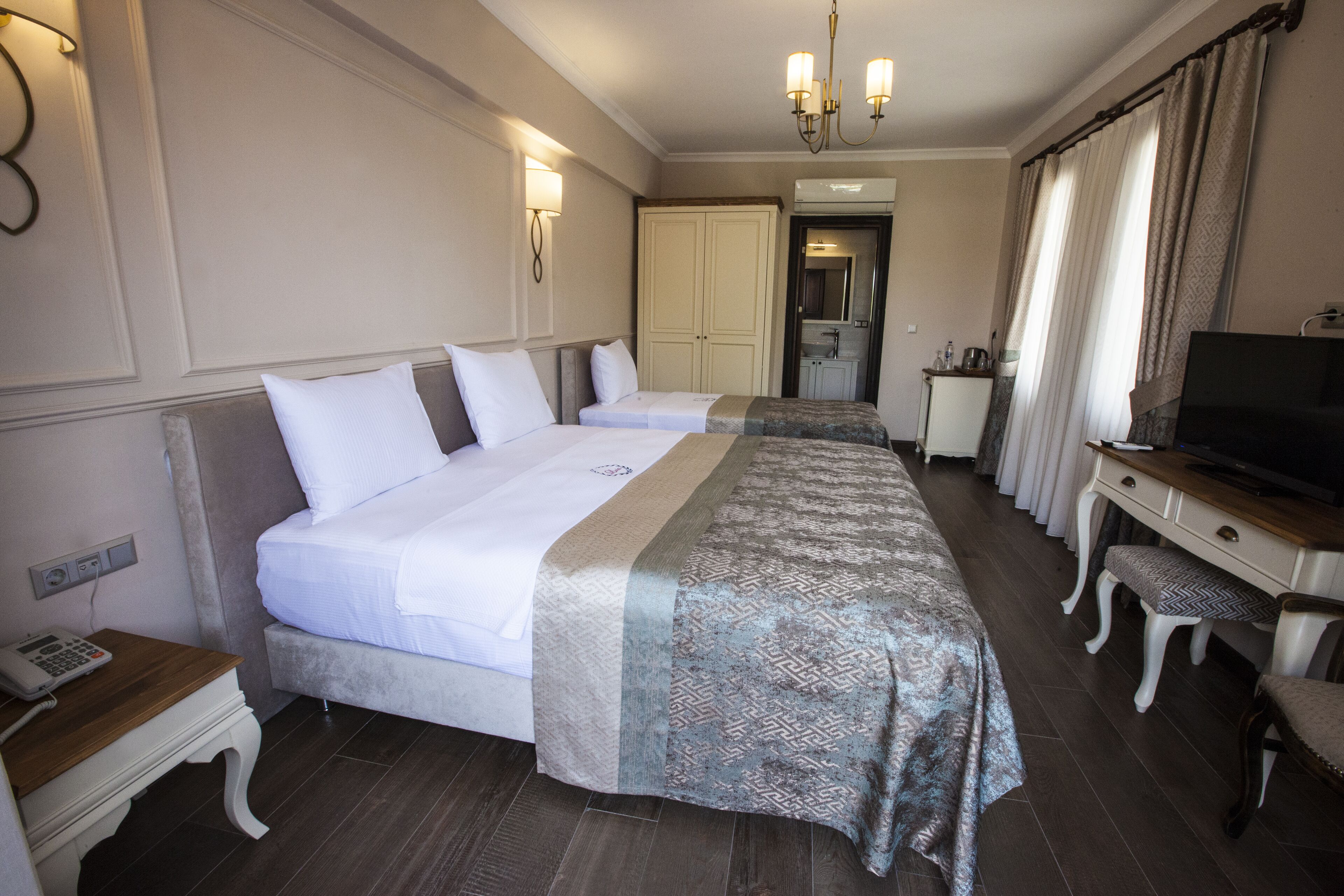 A hotel room with two beds, a desk with a television, a telephone, and a bathroom visible through an open door.