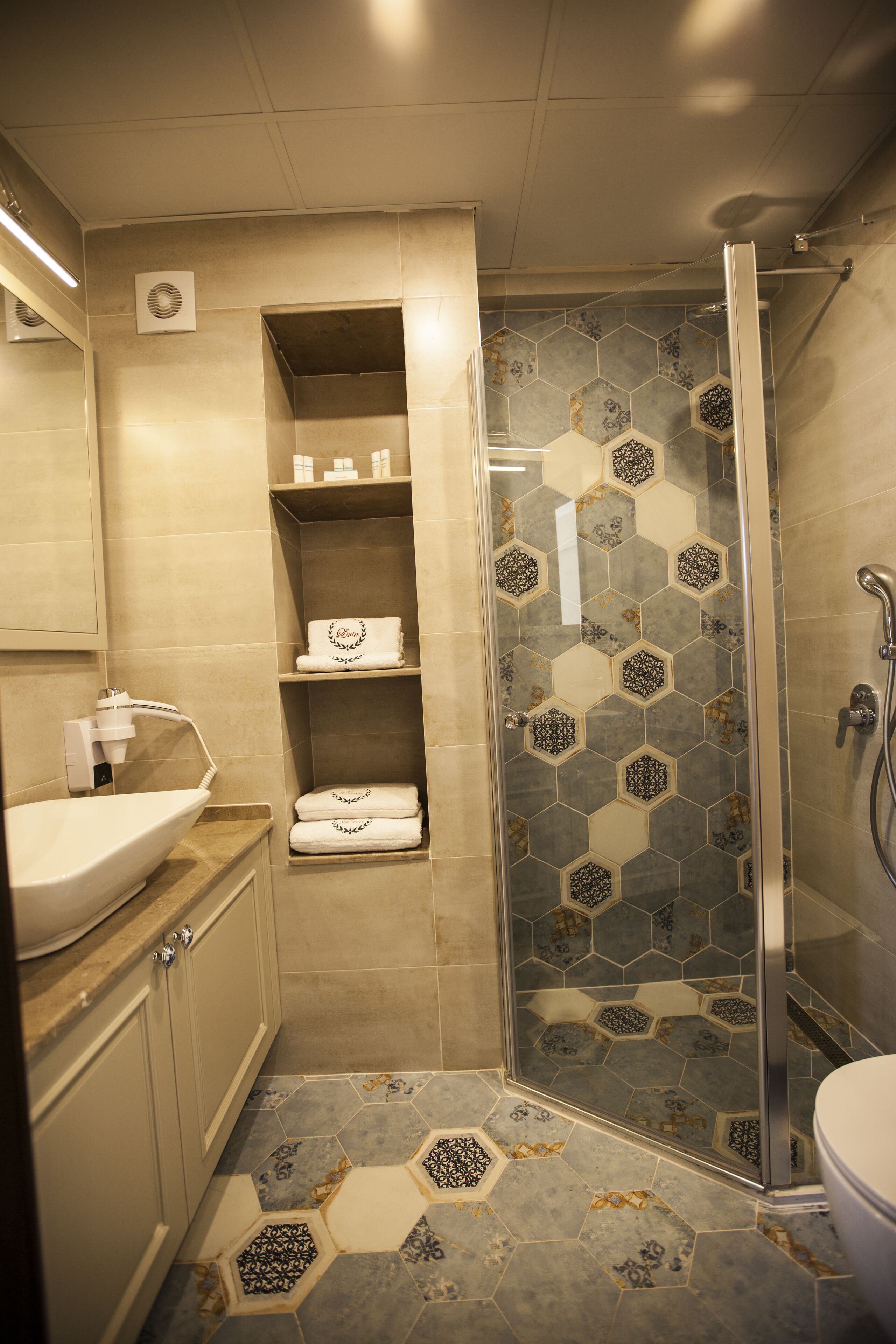 A bathroom with a glass-enclosed shower, a sink, and a vanity with storage shelves.