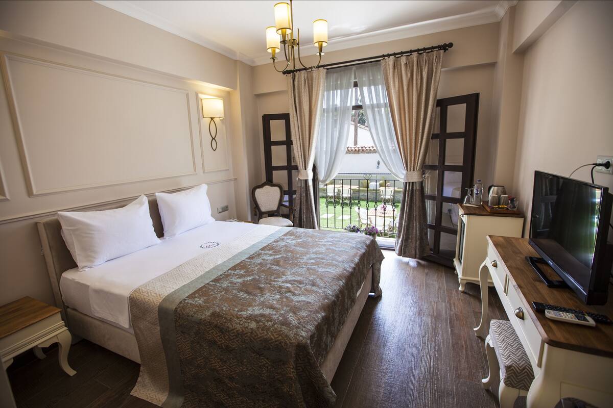 A hotel room with a large bed, a desk with a television, and a view of the outdoors.