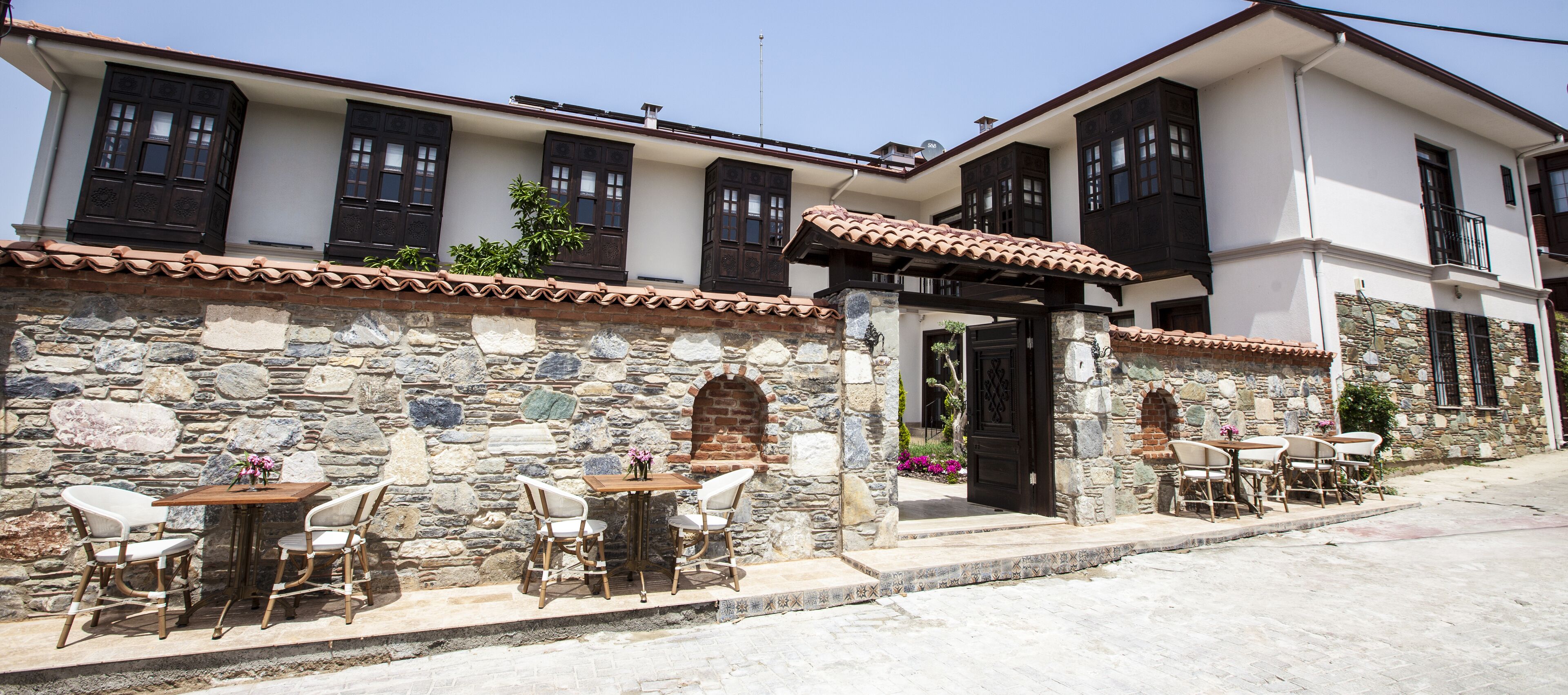Um edifício tradicional com paredes de pedra, telhado de telhas e várias janelas. Há mesas e cadeiras ao ar livre para refeições.