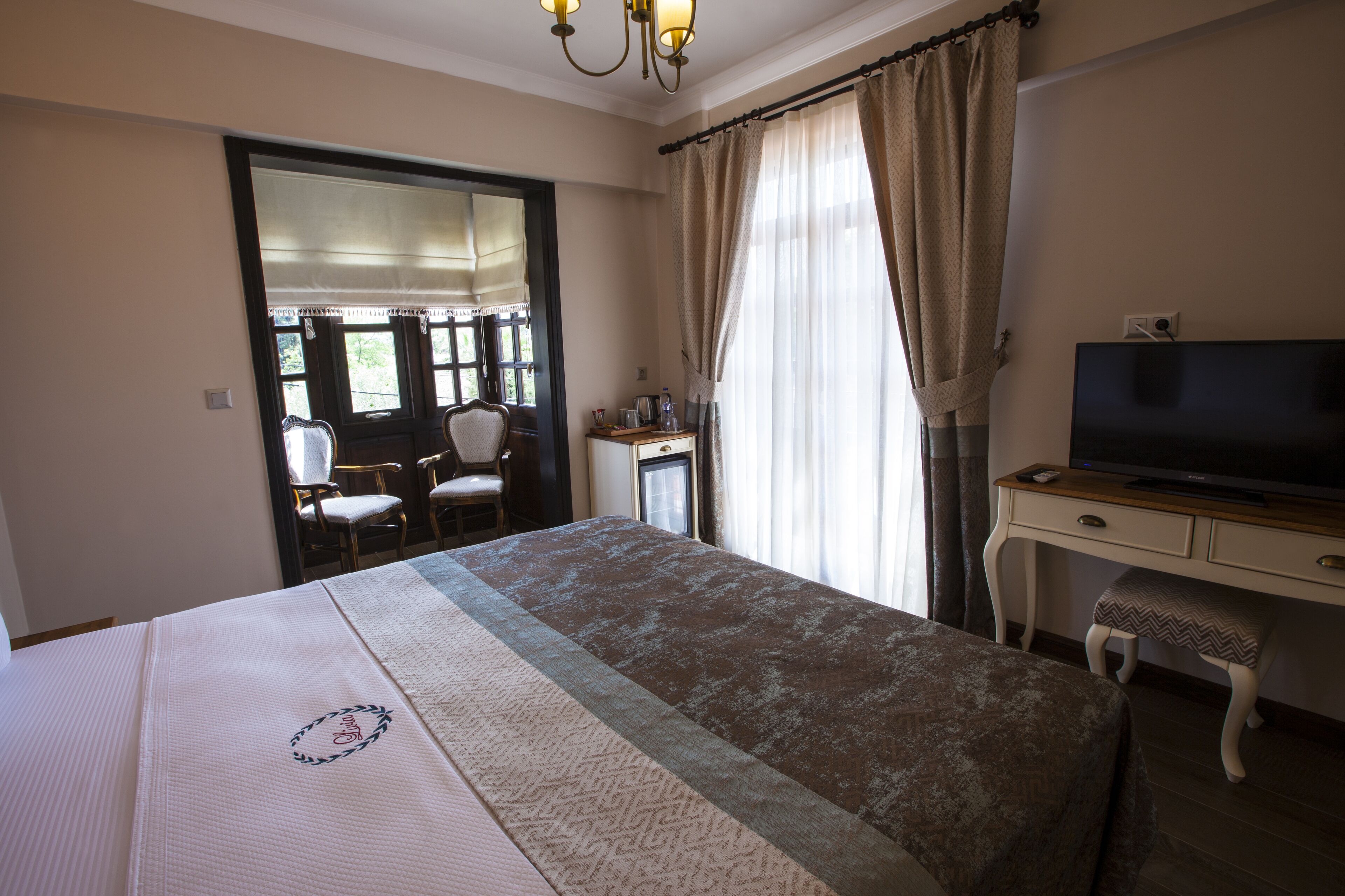 Una habitación de hotel con cama, escritorio con televisor, una silla y ventana con cortinas.