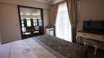 Una habitación de hotel con cama, escritorio con televisor, una silla y ventana con cortinas.