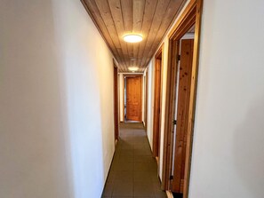 Kapea käytävä, jonka seinät ovat puuta ja lattia laatoitettu, ja joka johtaa käytävän päässä olevaan oveen.