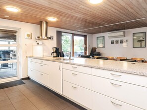 A modern kitchen with white cabinetry, a stainless steel range hood, and a large island with a sink. - 5 Star Holiday Home in Roslev (Roslev)