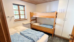 A dormitory room with bunk beds, a window, a white wardrobe, and a small shelf.