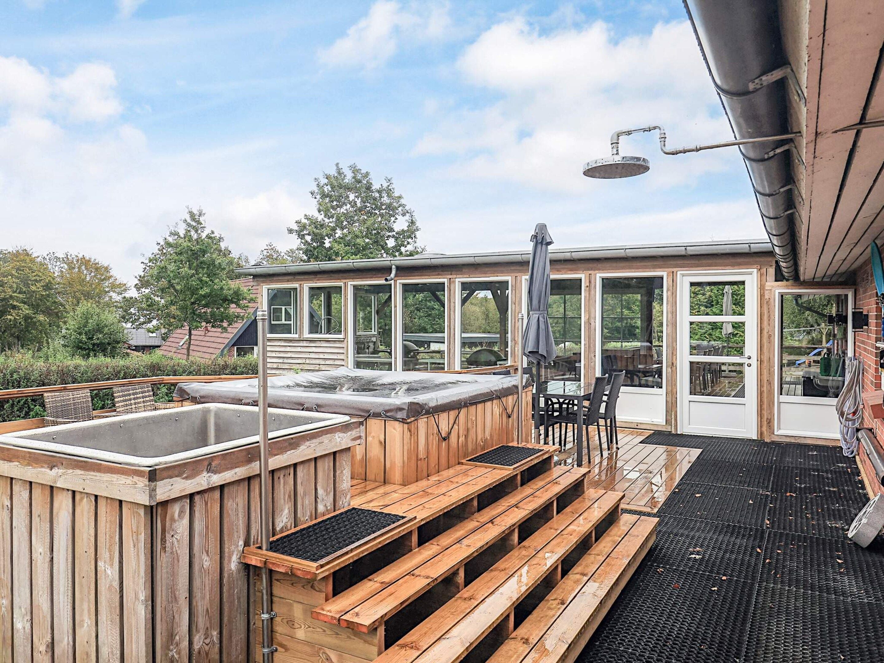 A wooden deck with a hot tub, outdoor seating, and a covered area with a table and chairs.