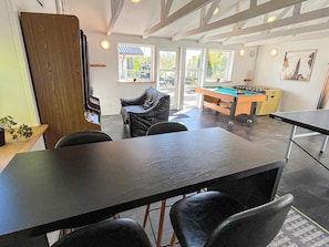 A room with a pool table, a foosball table, and a billiards table. There are two chairs and a sofa. The room has large windows and a view of the outside. - 5 Star Holiday Home in Roslev (Roslev)