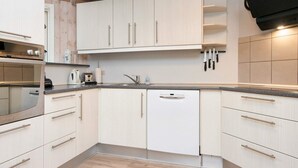 A modern kitchen with light wood cabinets, a built-in oven, a dishwasher, and a countertop with a sink and various kitchen items.
