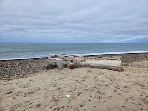 A beach with a large log in the sand and pebbles. - 7 Person Holiday Home in Frostrup (Frøstrup)
