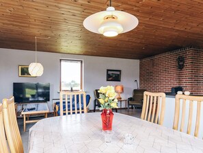 A dining area with a round table, chairs, a vase with flowers, a television, and a window. - 7 Person Holiday Home in Frostrup (Frøstrup)