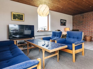 A modern living room with a TV, blue sofas, a wooden coffee table, and a brick wall.