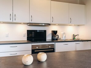 A modern kitchen with white cabinets, a black microwave, a coffee maker, and a stainless steel sink. - 7 Person Holiday Home in Frostrup (Frøstrup)