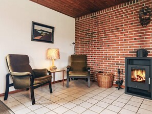 A living room with two armchairs, a table with a lamp, a fireplace, and a brick wall. - 7 Person Holiday Home in Frostrup (Frøstrup)