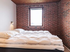A bedroom with a brick wall, a window, a bed with white bedding, and a floor lamp.